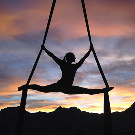 Mujer practicando yoga aéreo colgada de cintas durante el atardecer